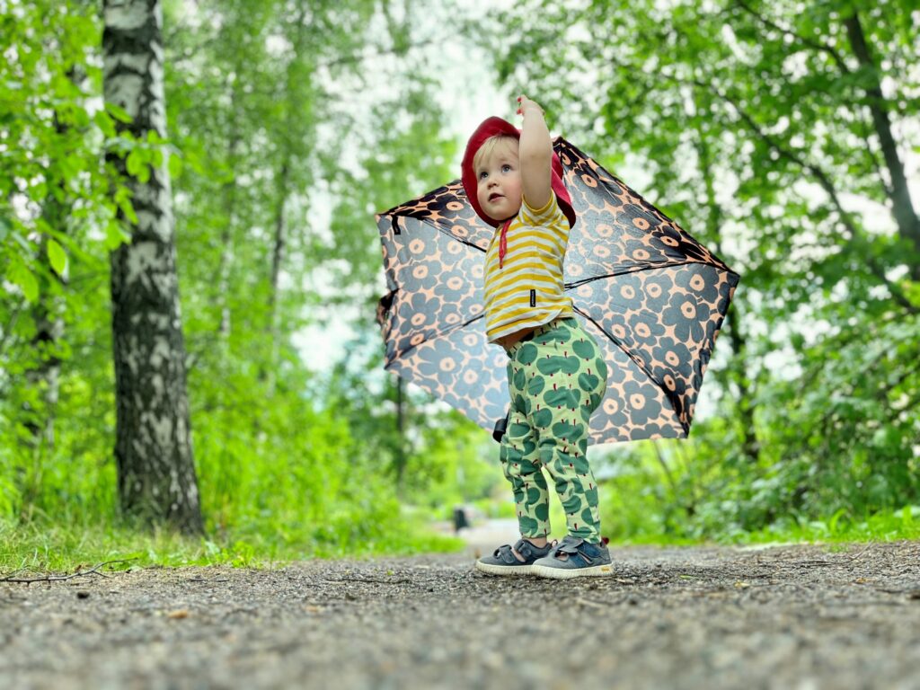 Lapsi sateenvarjon kanssa seisomassa koivukujalla.